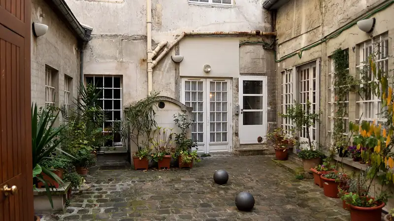 Cour intérieure pavée d'un immeuble ancien à Paris, avec des plantes en pot