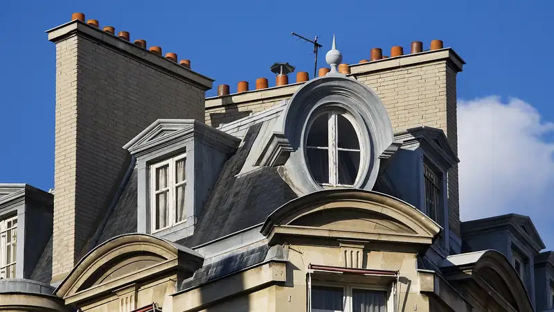 Toits de zinc et cheminées d'un immeuble parisien sous un ciel bleu